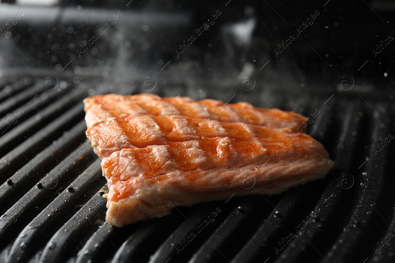 Photo of Tasty salmon cooking on electric grill, closeup