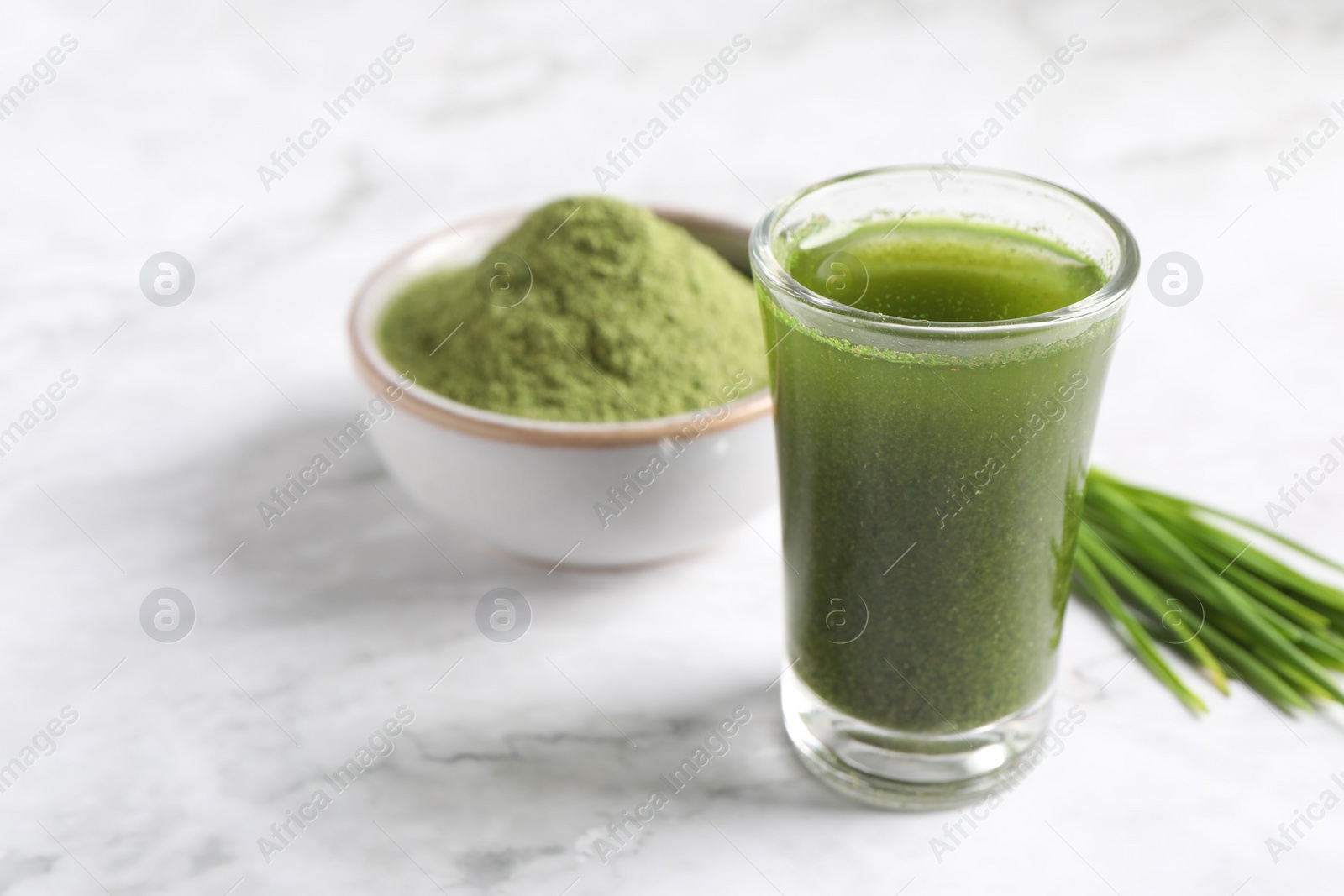 Photo of Wheat grass drink in shot glass on white marble table, closeup. Space for text