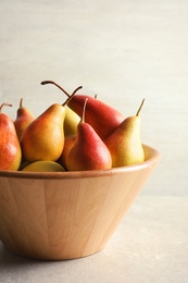 Photo of Bowl with ripe pears on table against light background