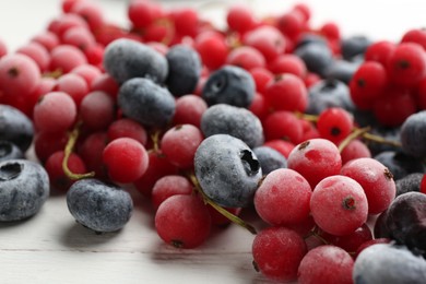 Photo of Tasty frozen blueberries and red currants on white wooden table, closeup