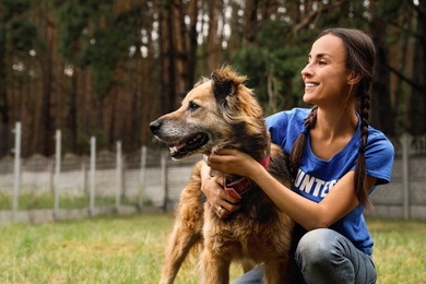 Photo of Female volunteer with homeless dog at animal shelter outdoors