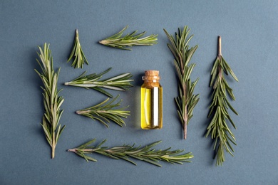 Photo of Bottle with rosemary essential oil and fresh herb on grey background, flat lay