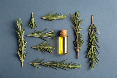 Bottle with rosemary essential oil and fresh herb on grey background, flat lay