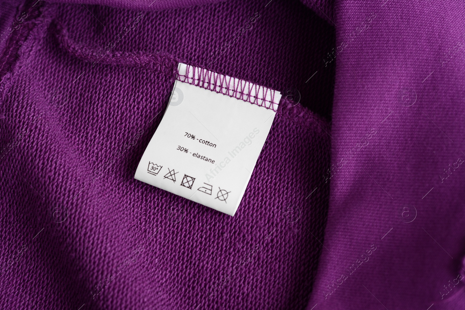 Photo of White clothing label with care information on purple garment, top view