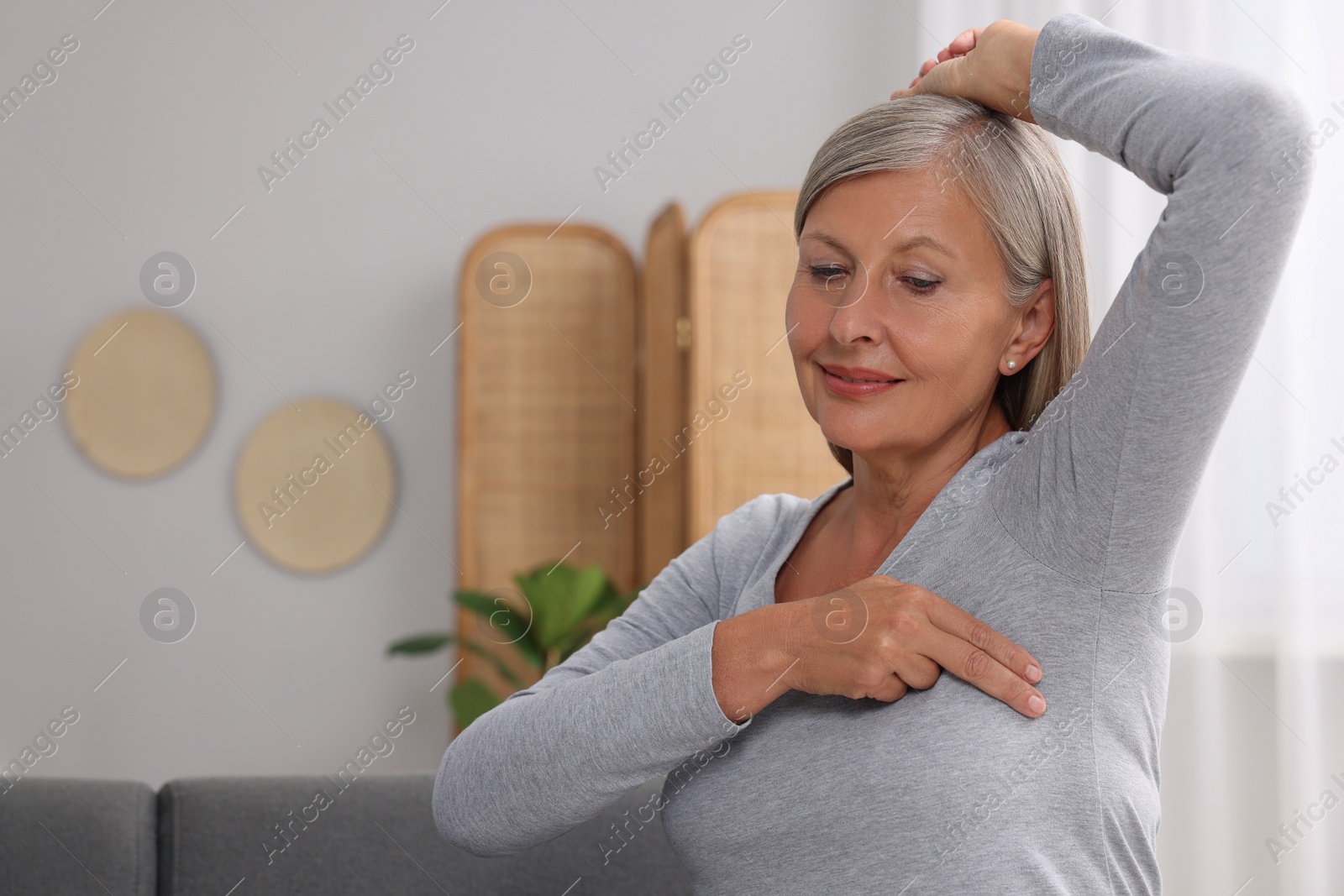 Photo of Beautiful senior woman doing breast self-examination at home, space for text