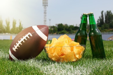 Photo of American football ball with beer and chips on green field grass in stadium