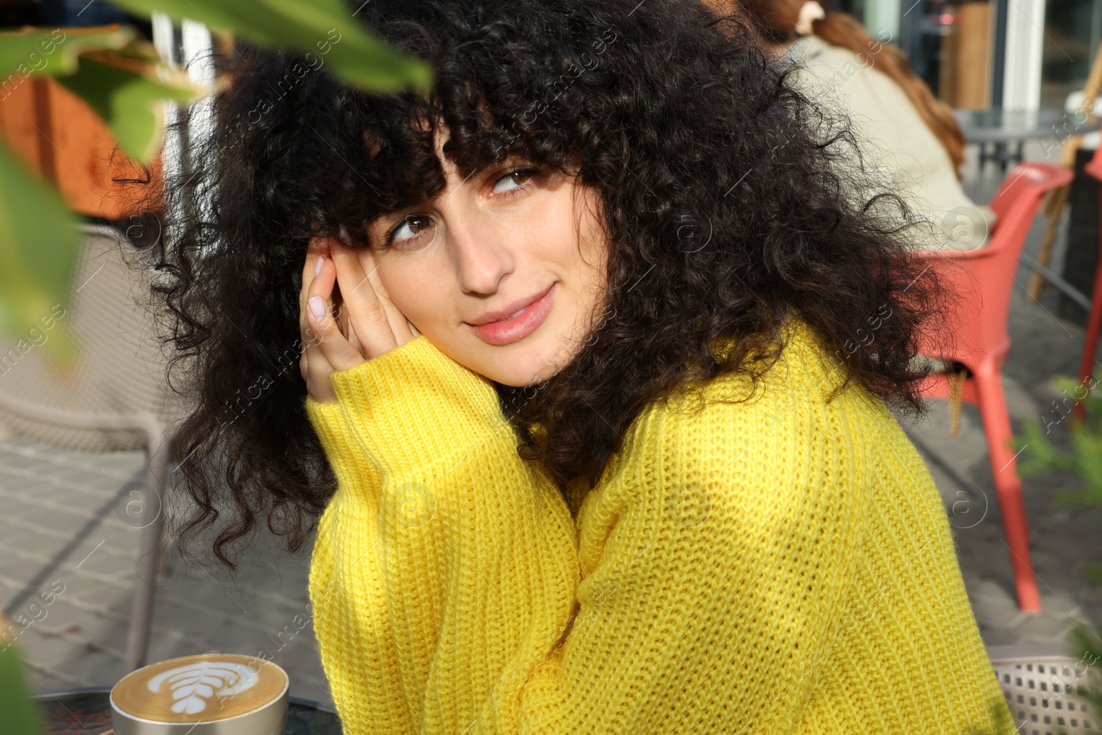 Photo of Young woman in stylish yellow sweater with cup of coffee at table outdoors