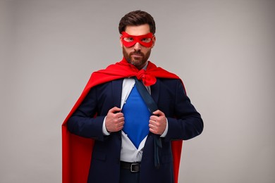 Confident businessman wearing superhero costume under suit on beige background