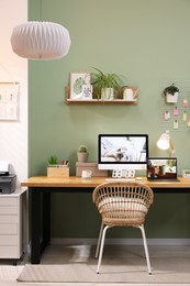 Stylish workplace with computer, laptop and lamp near olive wall at home