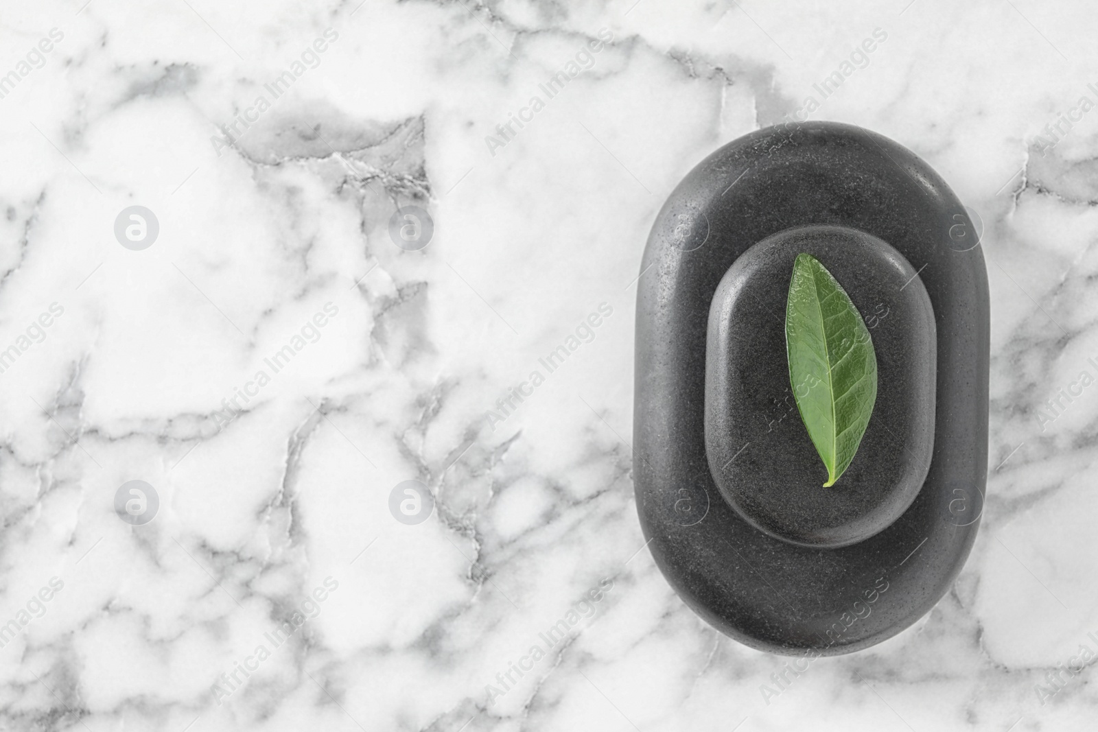 Photo of Spa stones and green leaf on marble table, top view with space for text