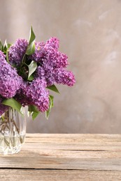 Beautiful lilac flowers in vase on wooden table, space for text