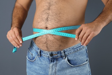 Overweight man with measuring tape on gray background, closeup