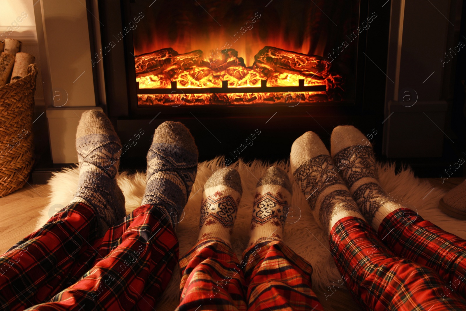 Photo of Family in warm socks resting near fireplace at home, closeup of legs