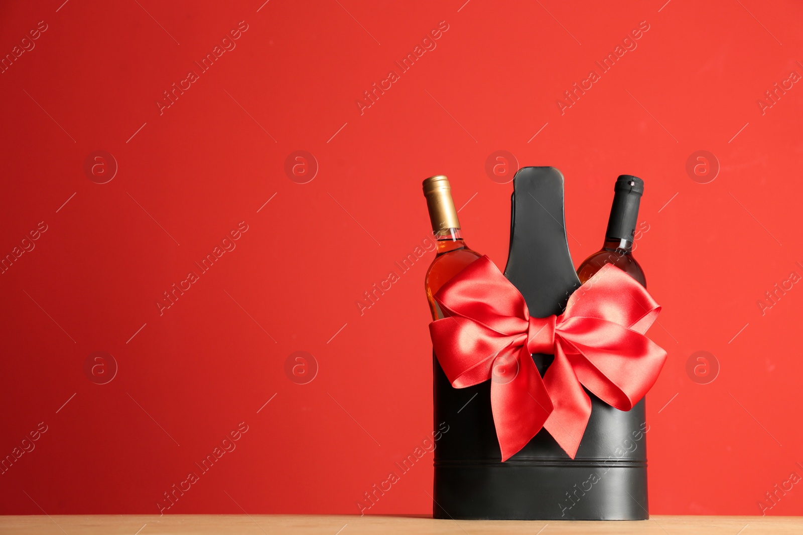 Photo of Bottles of wine in holder with bow on table against color background. Space for text