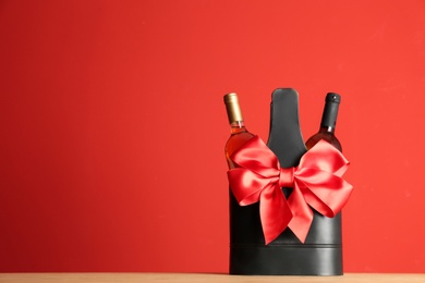 Photo of Bottles of wine in holder with bow on table against color background. Space for text