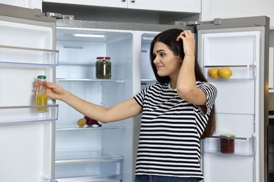 Photo of Upset woman near empty refrigerator in kitchen