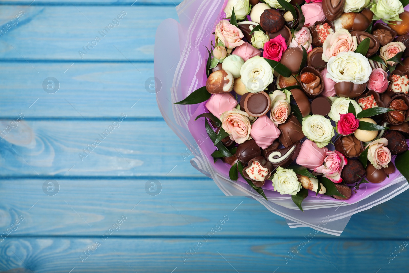 Photo of Beautiful bouquet of flowers and chocolate candies on light blue wooden table, top view. Space for text