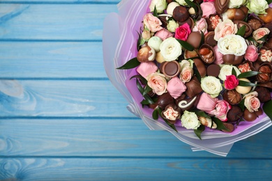 Beautiful bouquet of flowers and chocolate candies on light blue wooden table, top view. Space for text