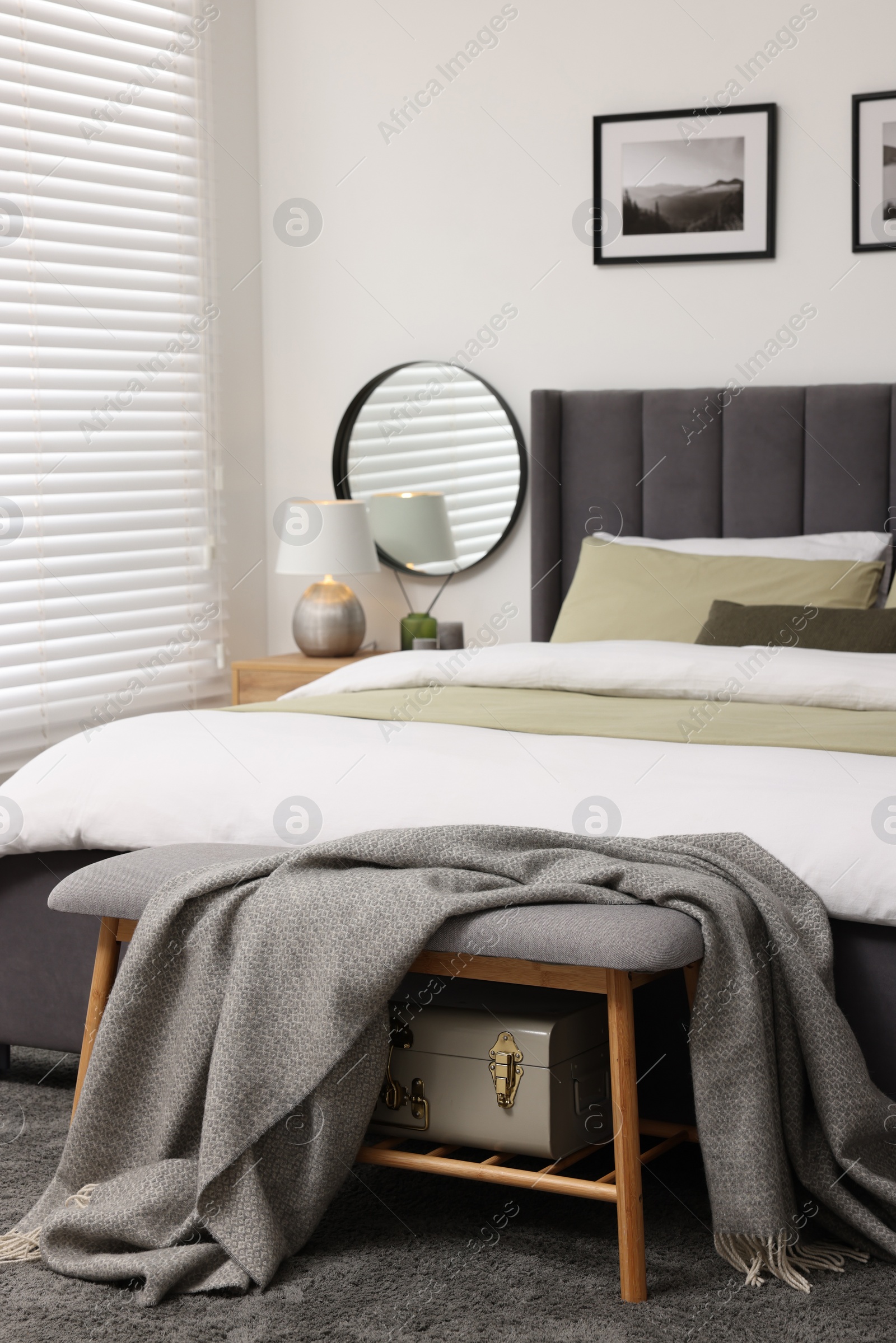 Photo of Horizontal blinds on window, comfortable bed and ottoman with blanket in room