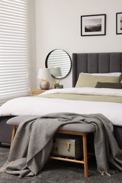 Horizontal blinds on window, comfortable bed and ottoman with blanket in room