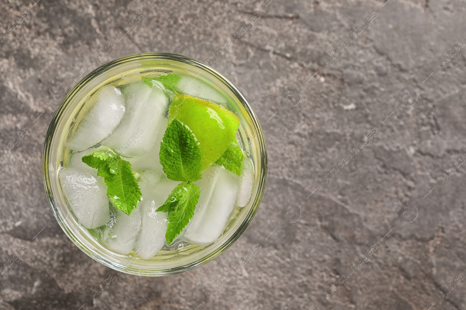Photo of Refreshing beverage with mint and lime in glass on grey background, top view