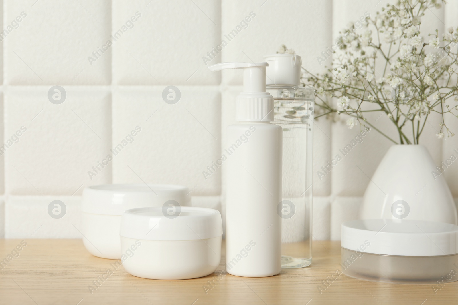 Photo of Bath accessories. Different personal care products and gypsophila flowers in vase on wooden table near white tiled wall