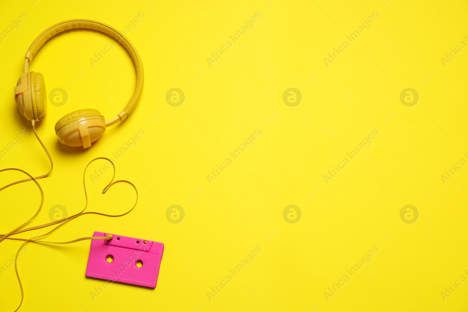 Photo of Heart made with cable of headphones and music cassette on yellow background, flat lay. Space for text