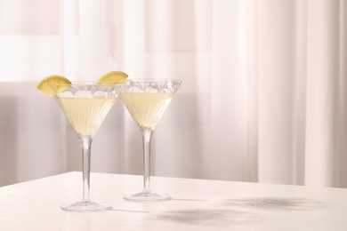 Photo of Elegant martini glasses with fresh cocktail and lemon slices on white table indoors. Space for text