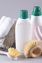 Bottles of cleaning product, brushes and rags on light background