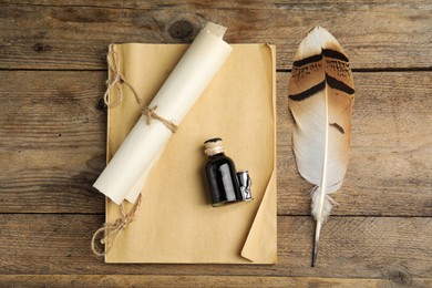 Feather pen, bottle of ink, notebook and parchment scroll on wooden table, flat lay