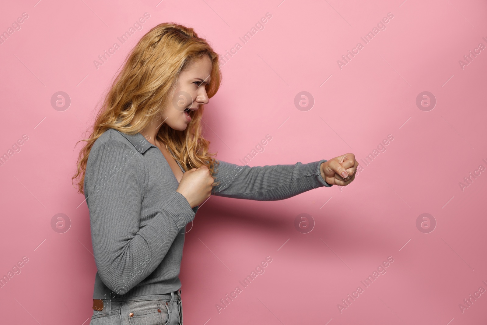 Photo of Angry young woman ready to fight on pink background