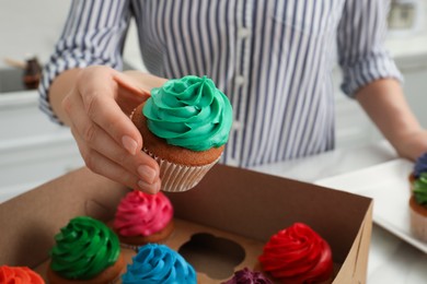 Woman holding delicious cupcake with turquoise cream at table indoors, closeup