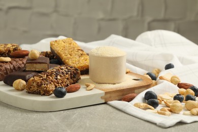 Photo of Different energy bars, nuts, blueberries and protein powder on grey table
