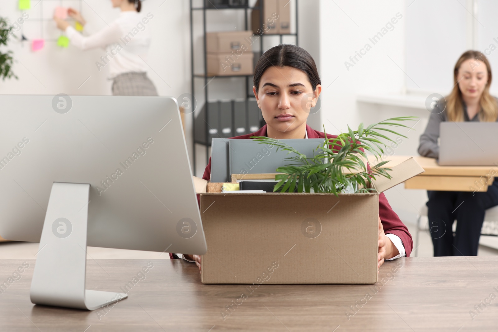 Photo of Unemployment problem. Frustrated woman with box of personal belongings at table in office