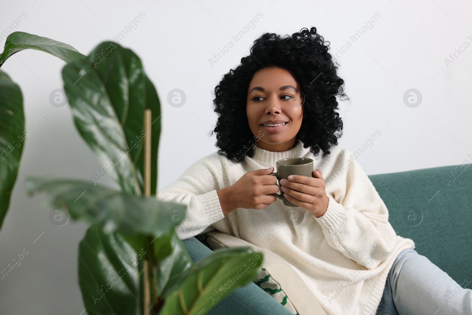 Photo of Relaxing atmosphere. Happy woman with cup of hot drink near beautiful houseplants indoors