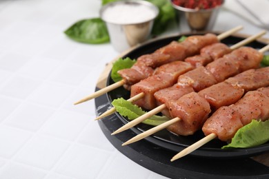 Photo of Wooden skewers with cut raw marinated meat on white tiled table, closeup. Space for text