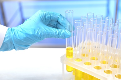 Photo of Laboratory assistant taking test tube with urine sample for analysis from holder on table, closeup