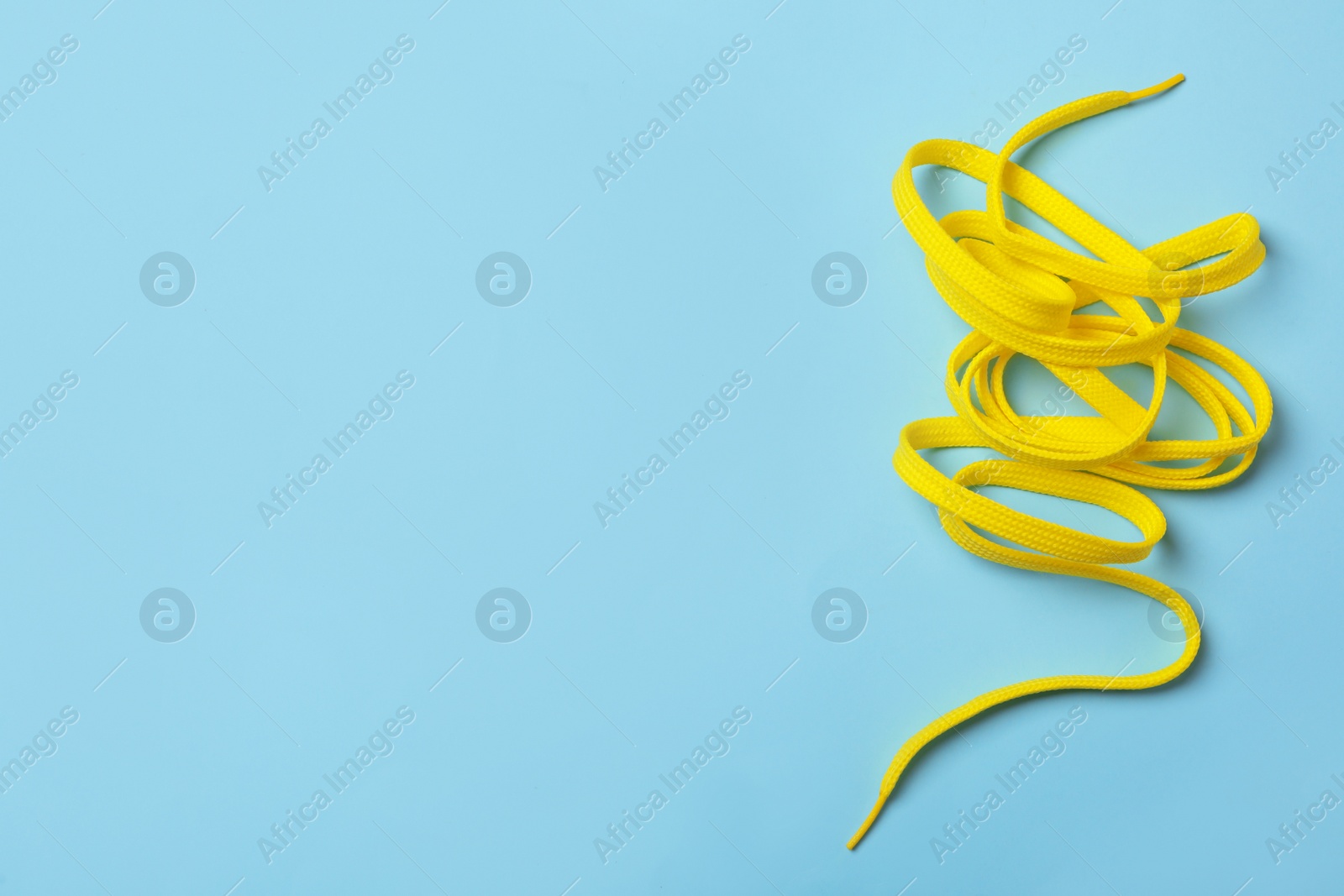 Photo of Yellow shoelace on light blue background, top view. Space for text