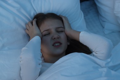 Little girl suffering from headache in bed at night