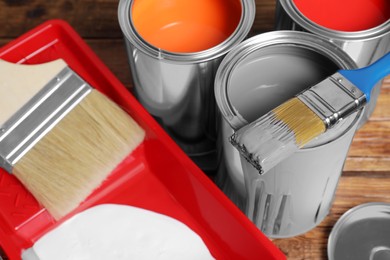 Photo of Cans of paints, brushes and tray on wooden background, closeup