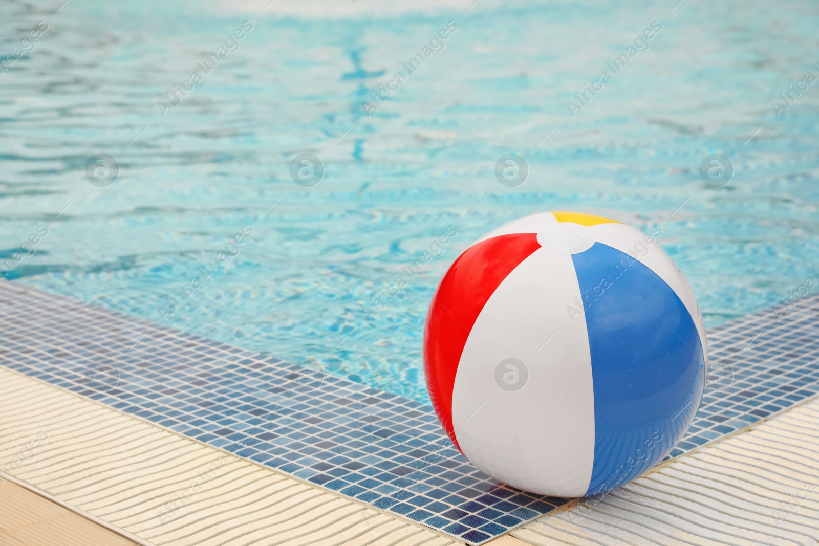 Photo of Inflatable colorful beach ball on edge of outdoor swimming pool, space for text