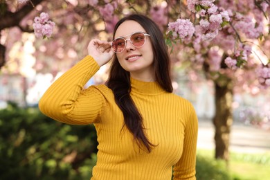 Photo of Beautiful woman in sunglasses near blossoming tree on spring day