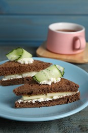 Photo of Plate of tasty sandwiches with cucumber and cream cheese on light blue wooden table