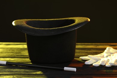 Photo of Magician's hat, wand and gloves on wooden table against black background