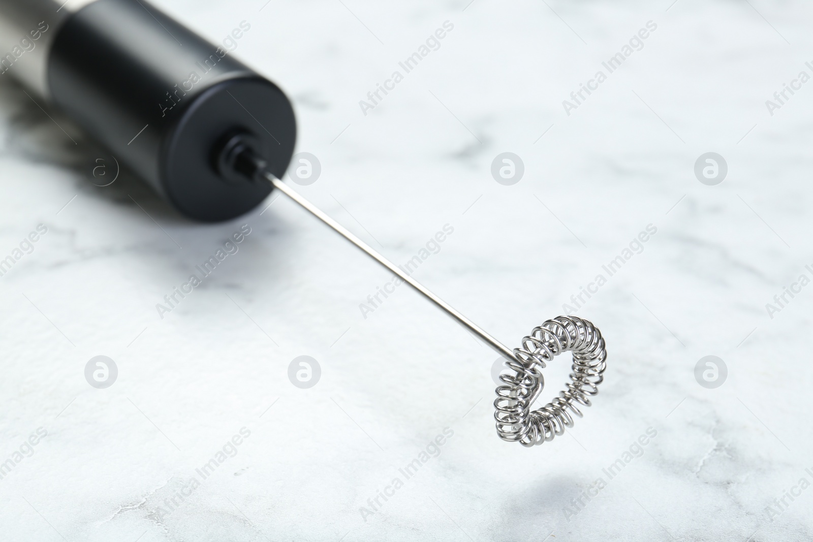 Photo of Black milk frother wand on white marble table, closeup