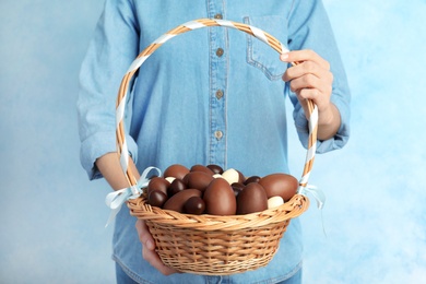 Photo of Woman holding wicker basket with chocolate Easter eggs on color background, closeup