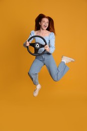 Photo of Excited young woman jumping with steering wheel on yellow background