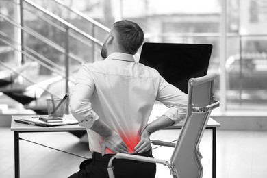 Image of Man suffering from back pain in office. Black and white effect with red accent