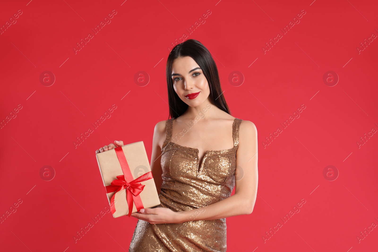 Photo of Woman in golden dress holding Christmas gift on red background