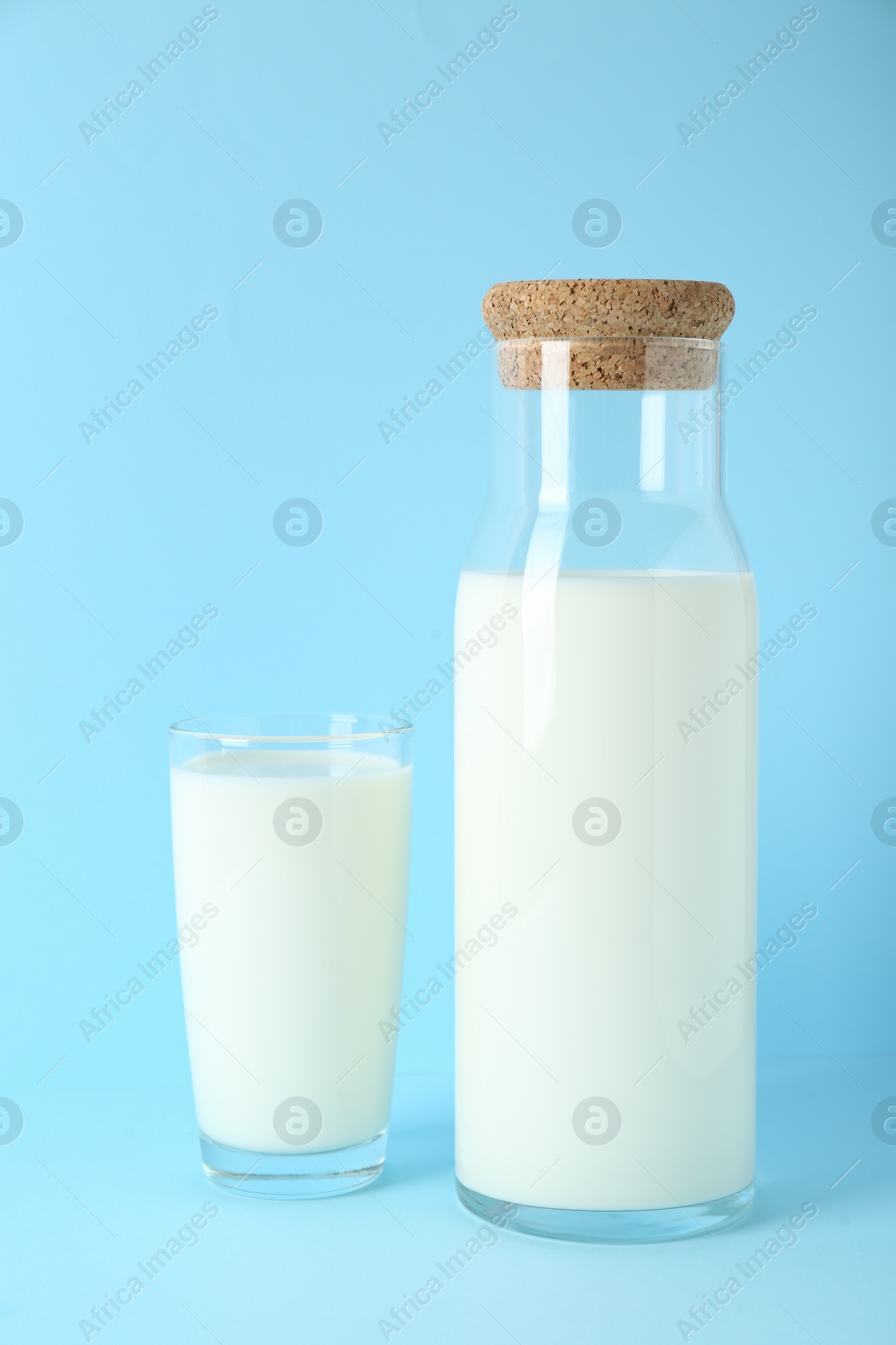 Photo of Carafe and glass of fresh milk on light blue background